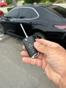 hand holding car key fob in front of vehicle for car key replacement and locksmith service