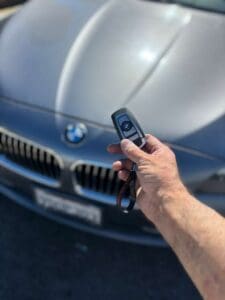 Automotive locksmith holding a BMW smart key fob remote in front of a vehicle during car key replacement or key fob programming service in Anaheim California